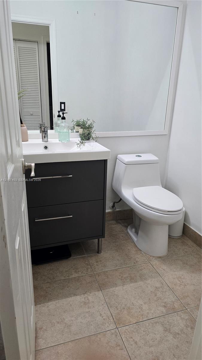 Dark gray dual-drawer vanity with a white countertop, rectangular integrated basin, one-piece toilet, large wall-mounted mirror, and tile flooring