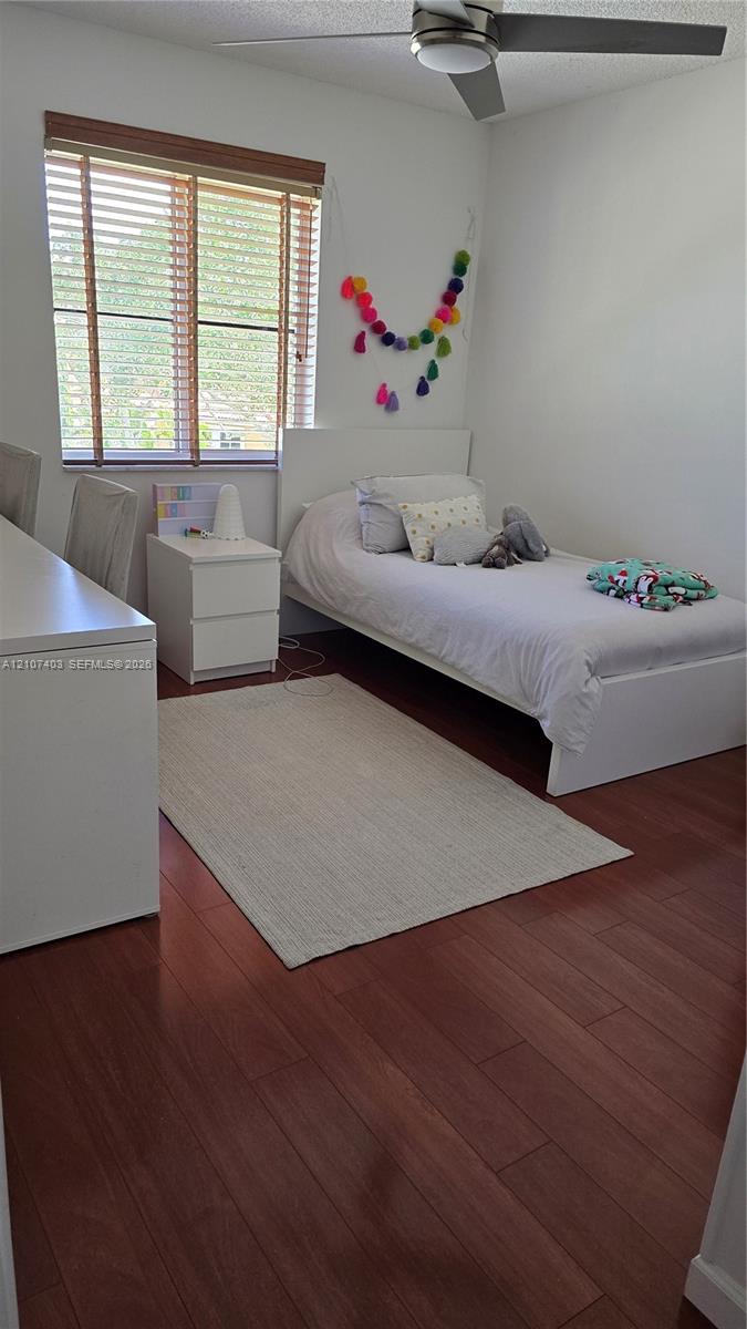 Bedroom featuring wood-finish flooring, a neutral color palette, a horizontal window with wood-slat blinds, and a ceiling-mounted light fixture with a fan