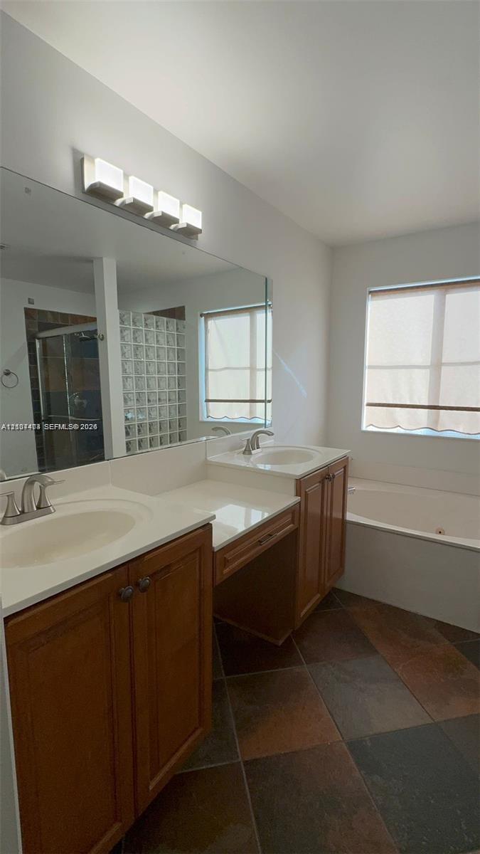 Dual-sink vanity with wood-finish cabinetry, solid-surface countertops, expansive wall mirror, and large-format tile flooring