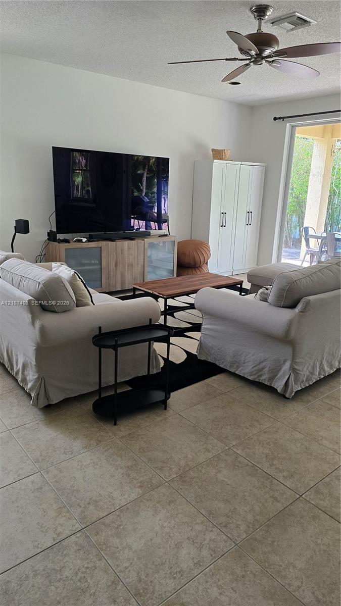 Neutral-toned tile flooring, ceiling fan with light fixture, and floor-to-ceiling glass sliding doors