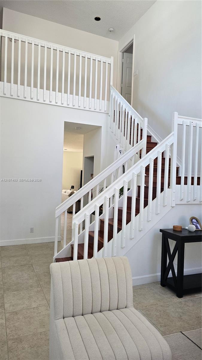 High-ceiling foyer featuring a staircase with wood-finish treads, white railings, and tile flooring