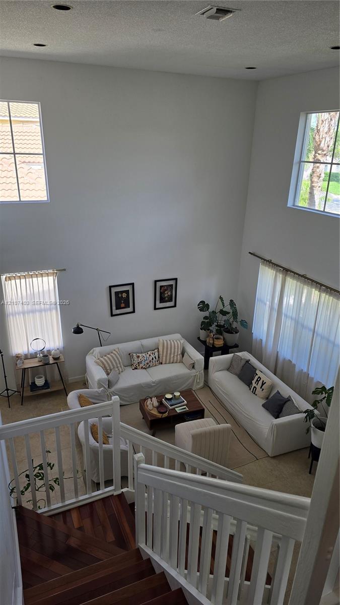 High-ceiling living area featuring multi-level windows, wood-finish staircase treads, and white vertical baluster railing High-ceiling living area featuring multi-level windows, wood-finish staircase treads, and white vertical baluster railing