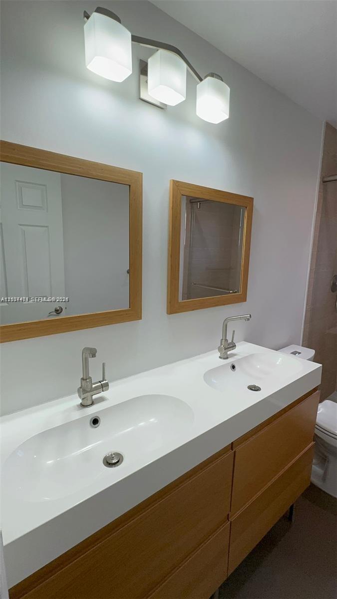 Double vanity with a white integrated sink countertop, wood-finish cabinetry, two square framed mirrors, and a brushed nickel three-light fixture