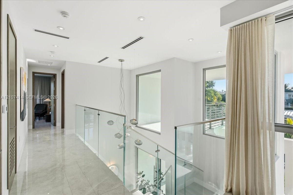 Hallway featuring polished stone flooring, glass panel railing, recessed ceiling lighting, and floor-to-ceiling windows
