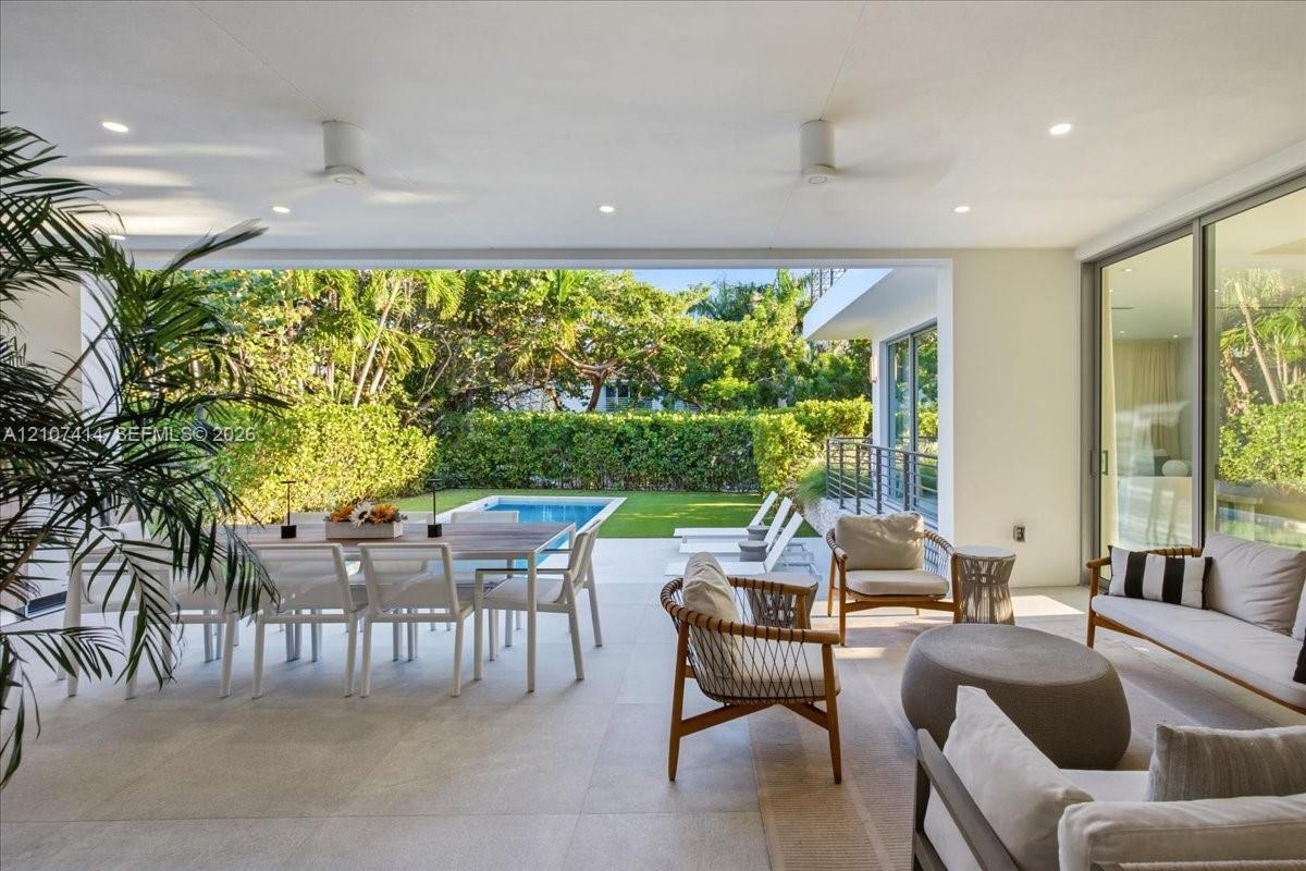 Covered patio featuring large-format stone-finish flooring, recessed lighting, ceiling fans, floor-to-ceiling glass sliding doors, and direct access to an outdoor swimming pool and manicured lawn
