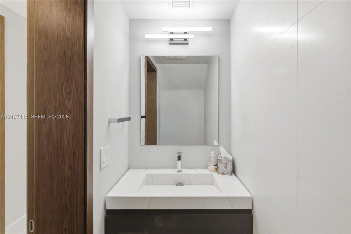 Floating vanity with an integrated basin, quartz countertop, minimalist wall-mounted lighting, frameless mirror, and large-format wall tile