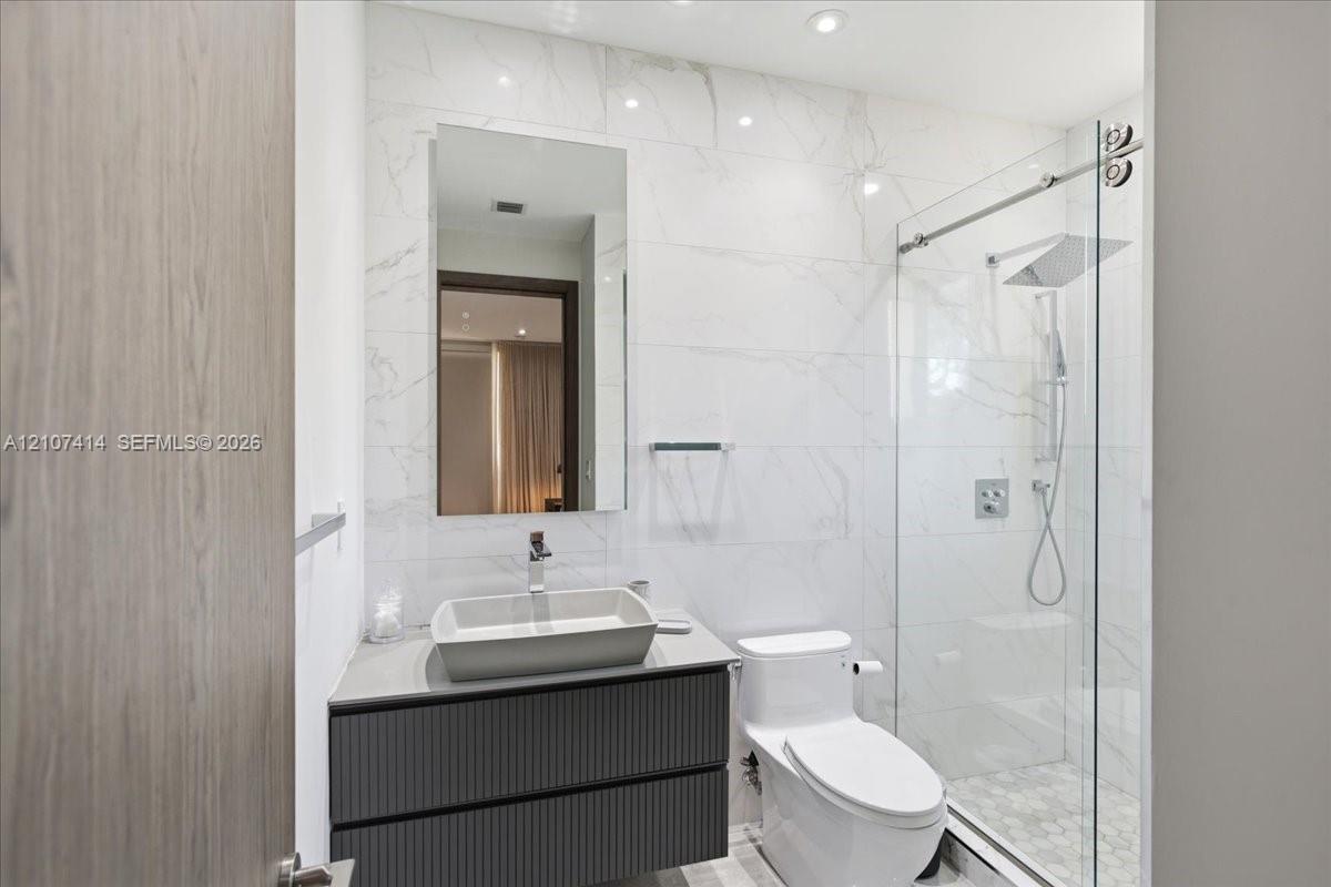 Floating vanity with a vessel sink, full-height tile wall, frameless glass shower enclosure, rainfall showerhead, and recessed lighting