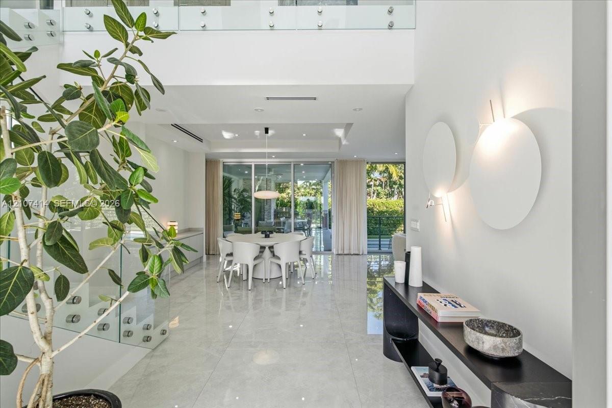 Double-height entryway featuring polished tile flooring, glass-panel staircase railing, recessed lighting, and wall-mounted circular accent fixtures Double-height entryway featuring polished tile flooring, glass-panel staircase railing, recessed lighting, and wall-mounted circular accent fixtures