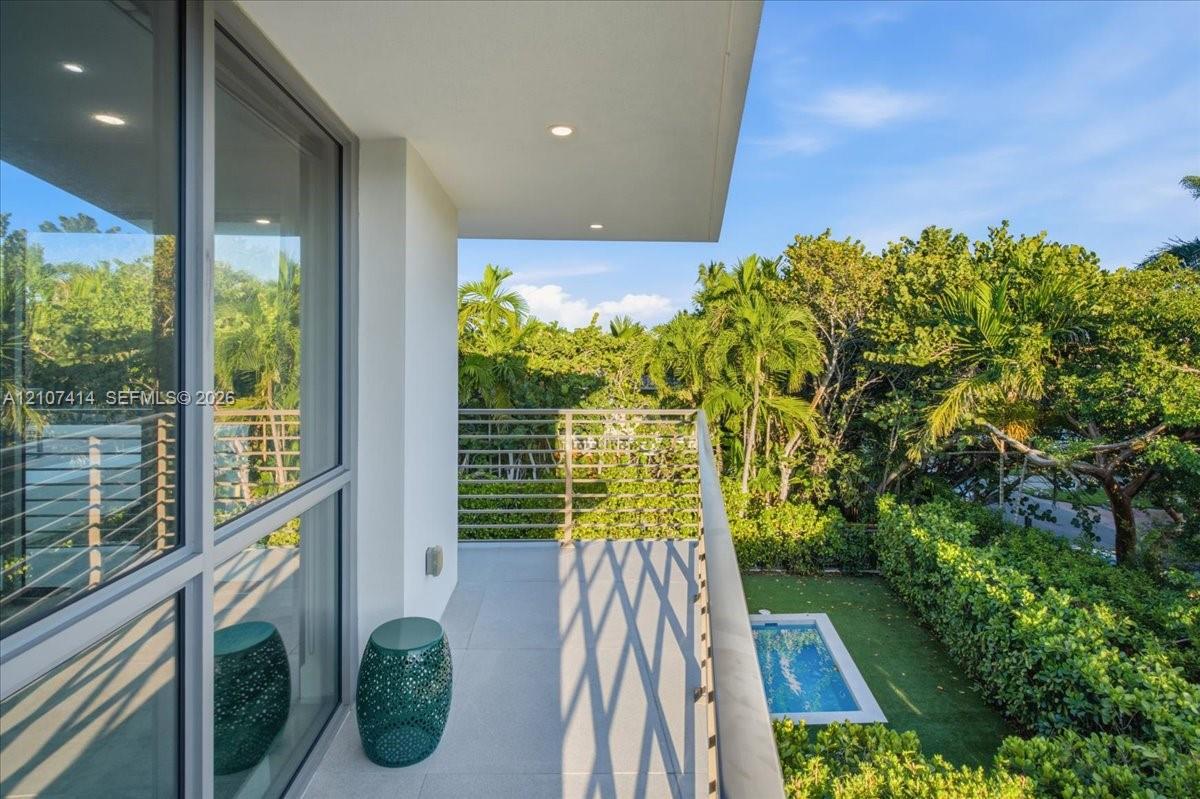 Covered balcony featuring tile flooring, horizontal cable railing, recessed lighting, and floor-to-ceiling glass paneling overlooking a private pool and manicured landscaping