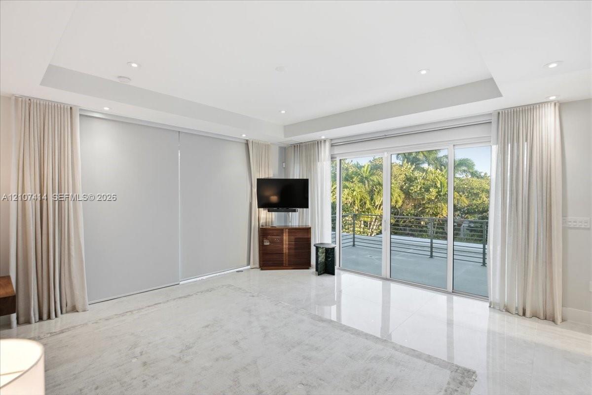 Tray ceiling with recessed lighting, large format tile flooring, and sliding glass doors opening to a balcony with metal railing