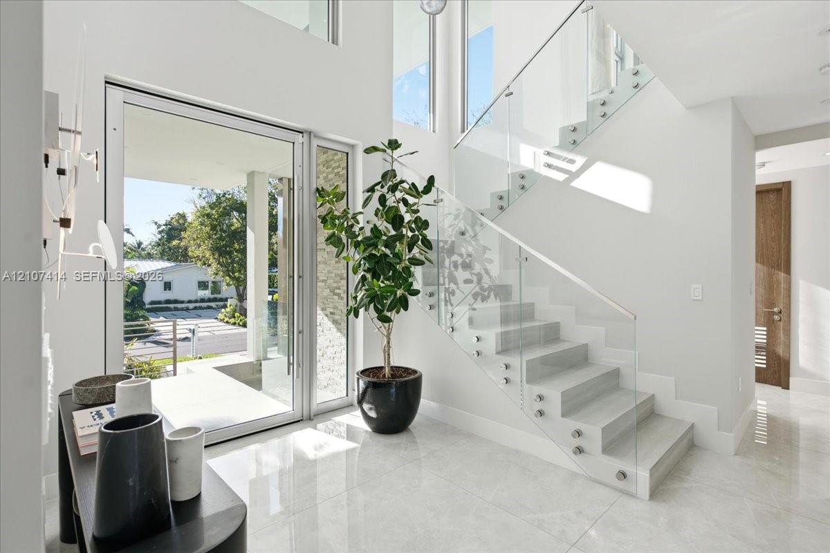Entryway featuring polished stone flooring, a multi-story ceiling, floor-to-ceiling windows, and a floating staircase with glass panel railings Entryway featuring polished stone flooring, a multi-story ceiling, floor-to-ceiling windows, and a floating staircase with glass panel railings