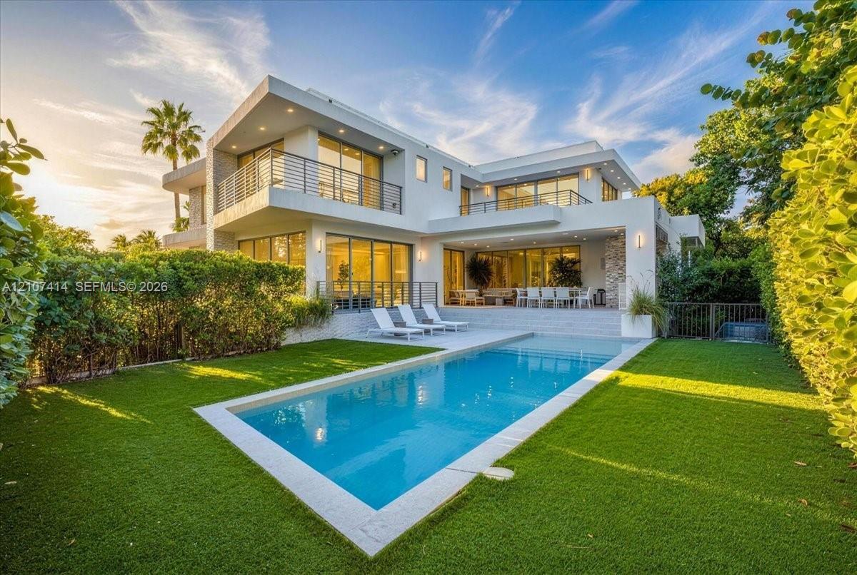 Modern two-story architectural exterior featuring expansive glass sliding doors, multiple balconies with metal railings, a rectangular swimming pool, and stone facade accents Modern two-story architectural exterior featuring expansive glass sliding doors, multiple balconies with metal railings, a rectangular swimming pool, and stone facade accents