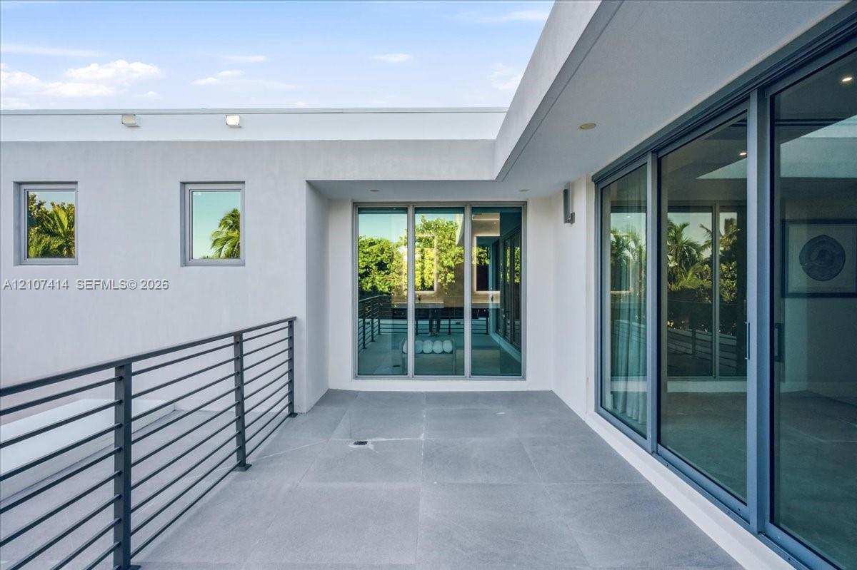Modern balcony featuring expansive stone-tile flooring, floor-to-ceiling glass sliding doors, and a sleek metal horizontal-bar railing