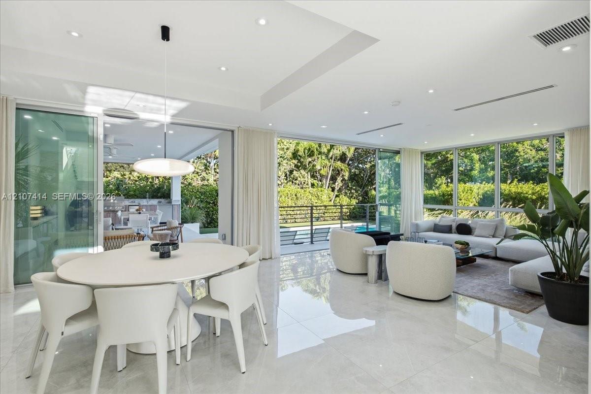 Open-concept living space featuring floor-to-ceiling glass sliding doors, polished tile flooring, recessed ceiling lighting, and a tray ceiling design