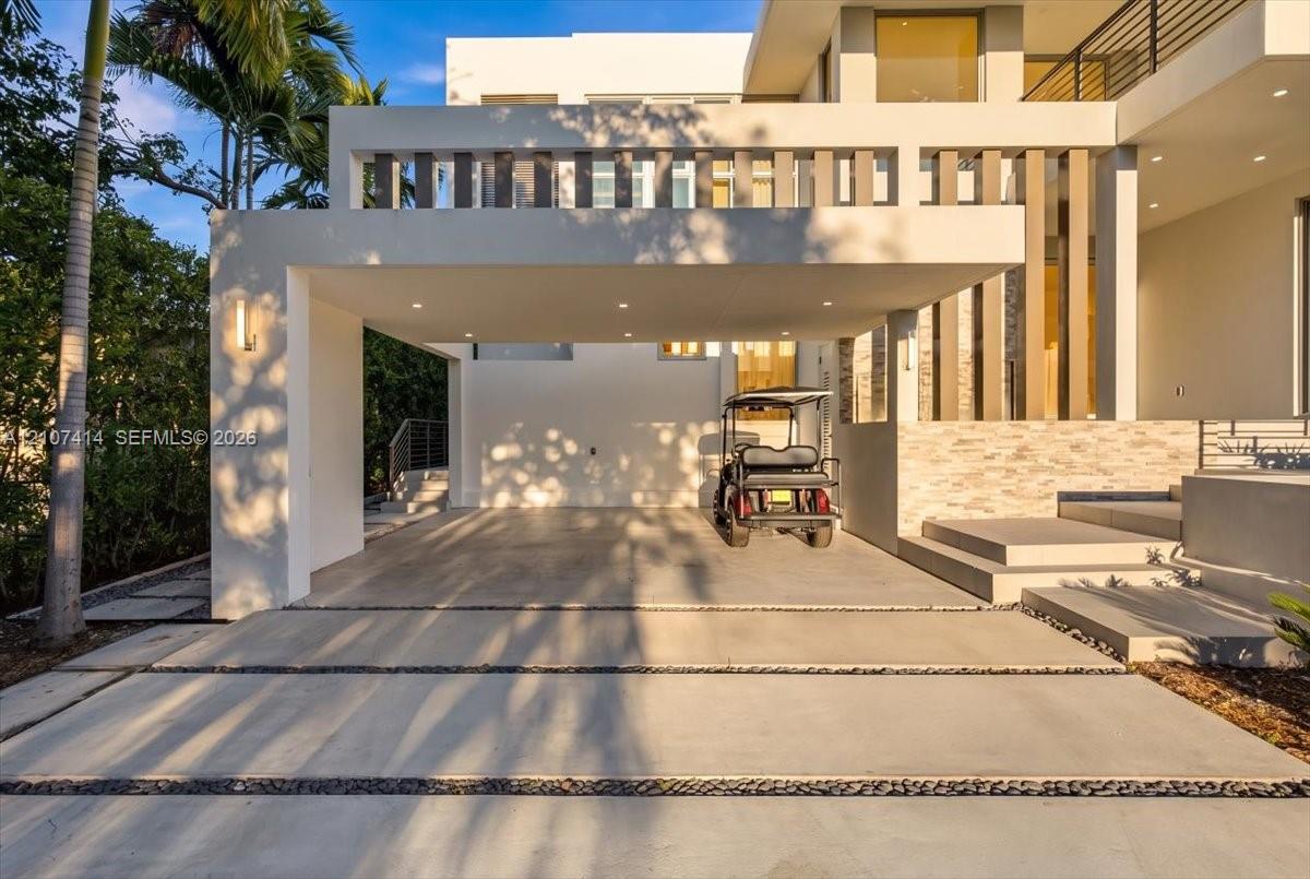 Modern architectural facade featuring a covered porte-cochre, recessed lighting, stacked stone exterior detailing, and a concrete driveway with decorative rock inlay Modern architectural facade featuring a covered porte-cochre, recessed lighting, stacked stone exterior detailing, and a concrete driveway with decorative rock inlay