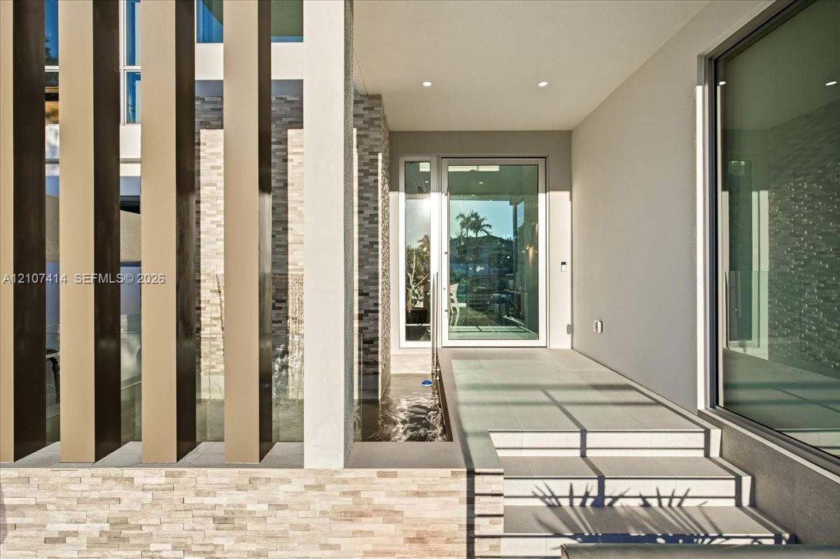 Contemporary entryway featuring vertical architectural screening, tiered stone masonry, recessed ceiling lighting, a water feature, and a glass-paneled entry door Contemporary entryway featuring vertical architectural screening, tiered stone masonry, recessed ceiling lighting, a water feature, and a glass-paneled entry door