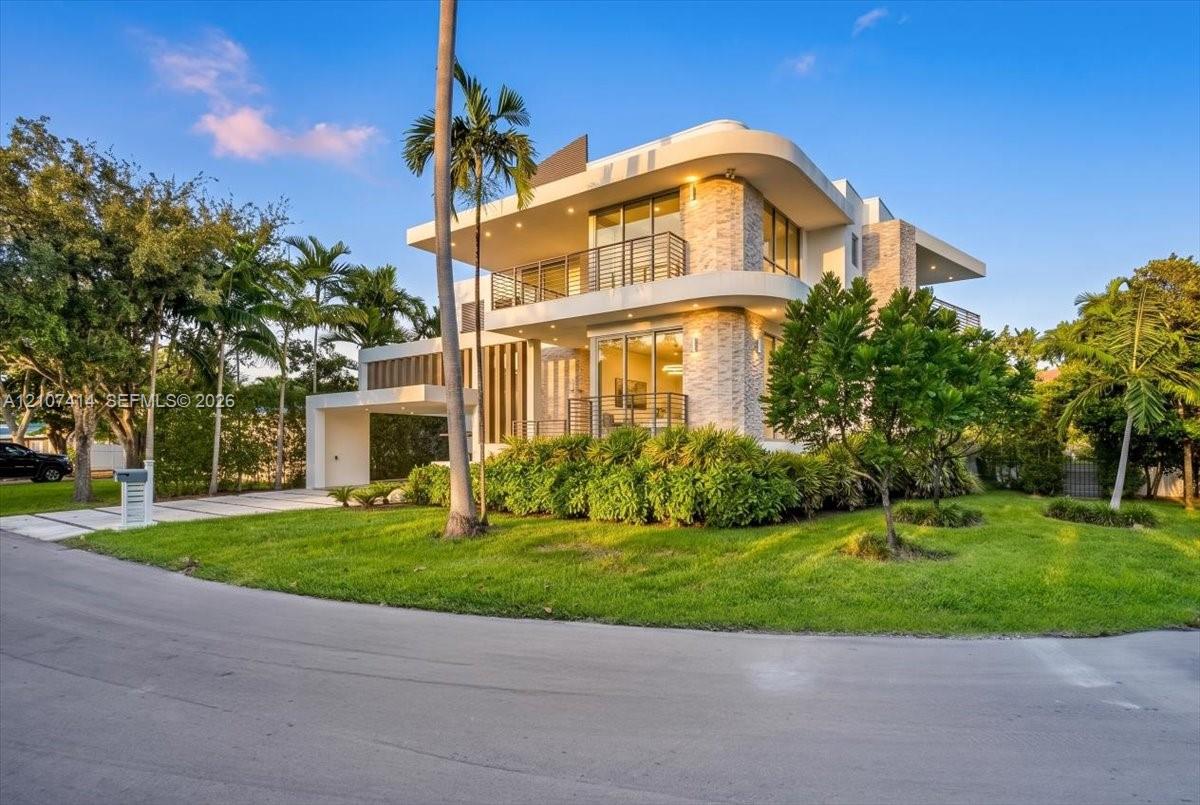 Modern multi-level exterior featuring curved architectural lines, stone-accented facade, expansive glass sliding doors, integrated balcony railings, and a covered porte-cochre Modern multi-level exterior featuring curved architectural lines, stone-accented facade, expansive glass sliding doors, integrated balcony railings, and a covered porte-cochre