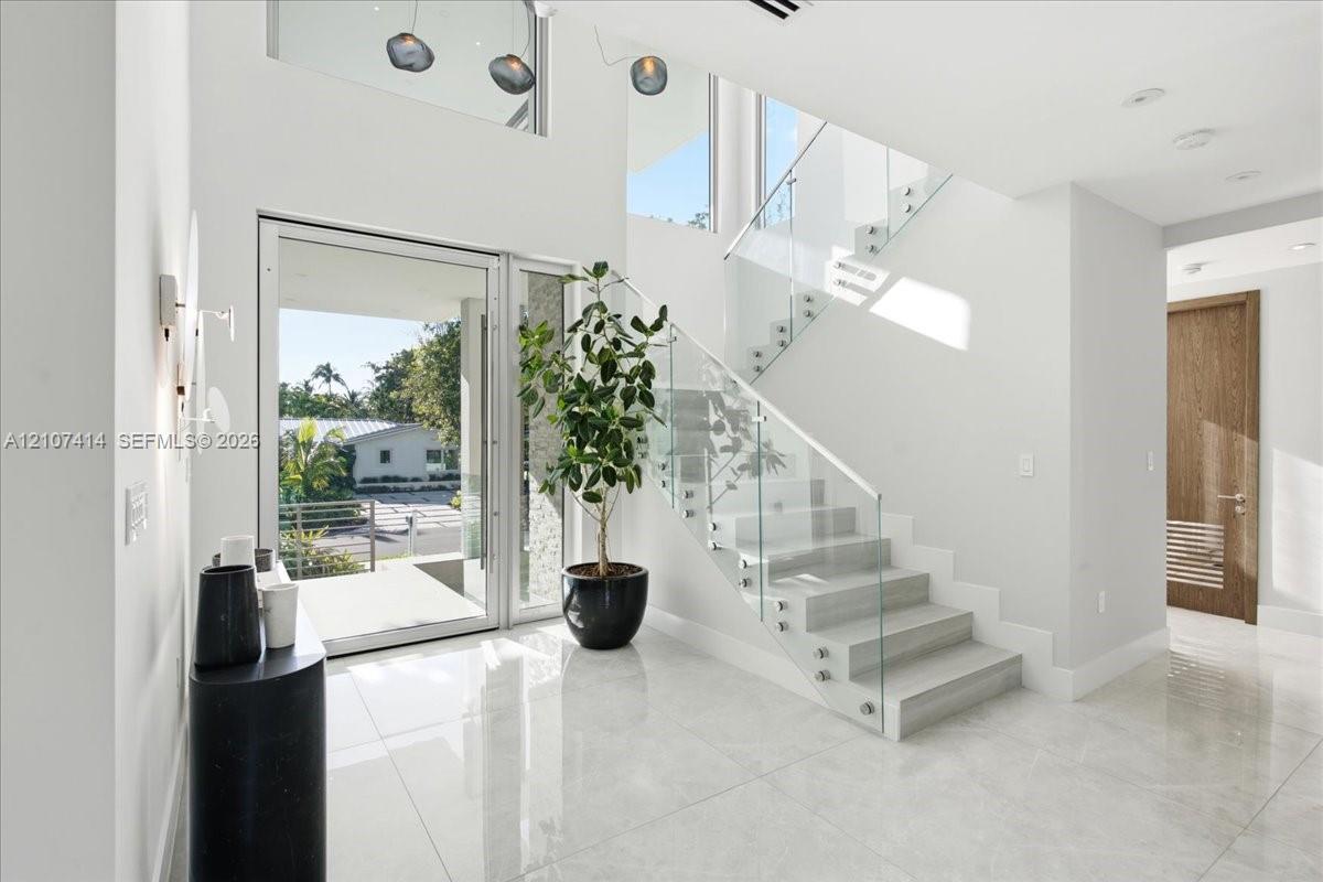 Grand entryway featuring high ceilings, large-format tile flooring, a glass-railed staircase, and a floor-to-ceiling glass-paneled front door