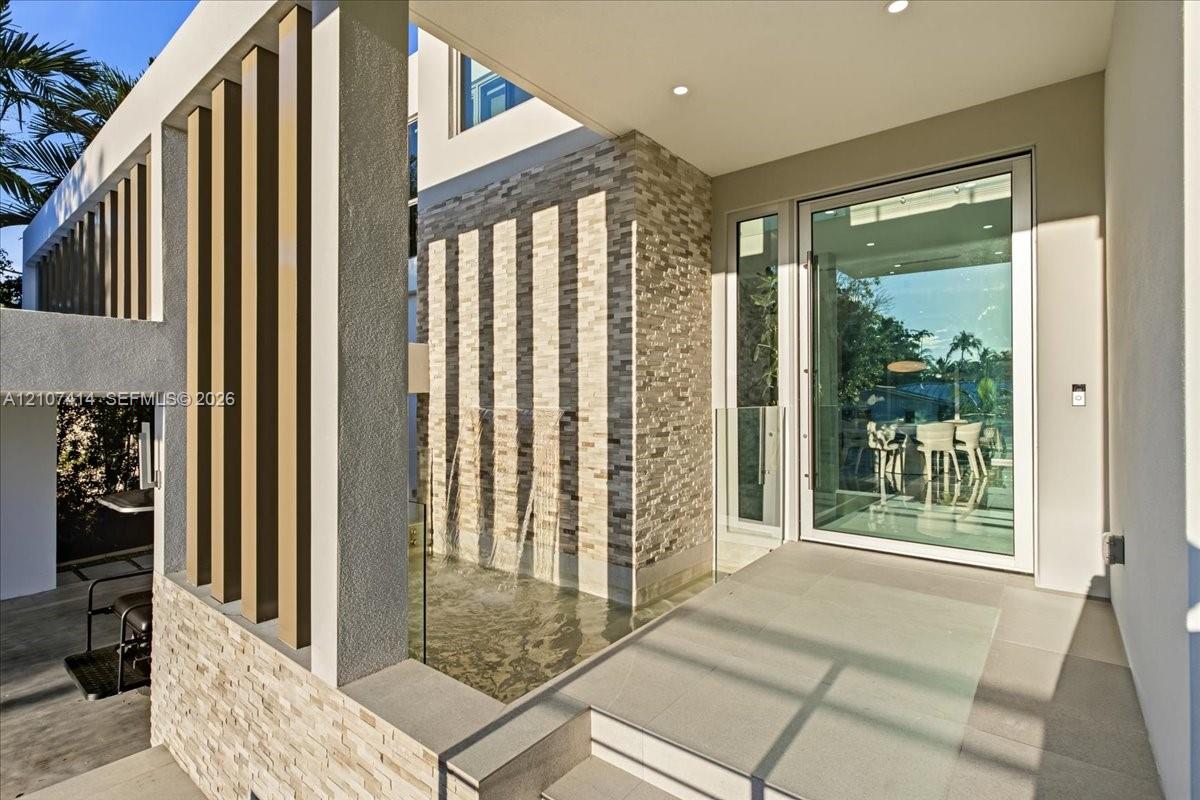 Modern entryway featuring a stacked stone facade, vertical architectural slats, an integrated water feature, recessed ceiling lighting, and a full-height glass-paneled entry door Modern entryway featuring a stacked stone facade, vertical architectural slats, an integrated water feature, recessed ceiling lighting, and a full-height glass-paneled entry door