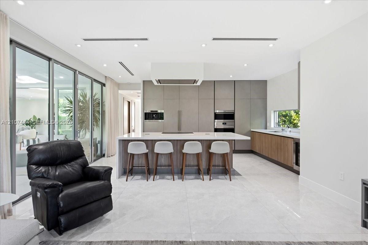 Chefs kitchen featuring full-height matte cabinetry, a waterfall-edge stone island, built-in stainless steel appliances, polished stone flooring, and expansive floor-to-ceiling glass sliding doors