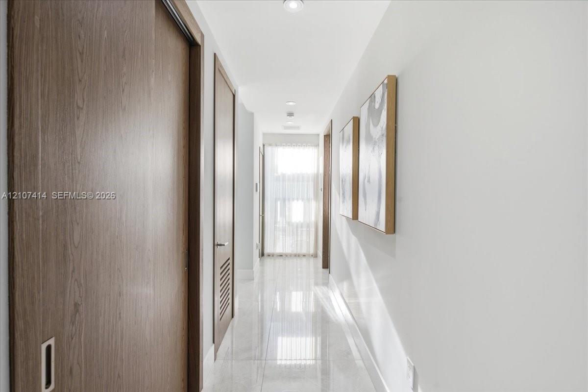 Hallway featuring polished tile flooring, recessed ceiling lighting, and wood-finish doors with integrated hardware