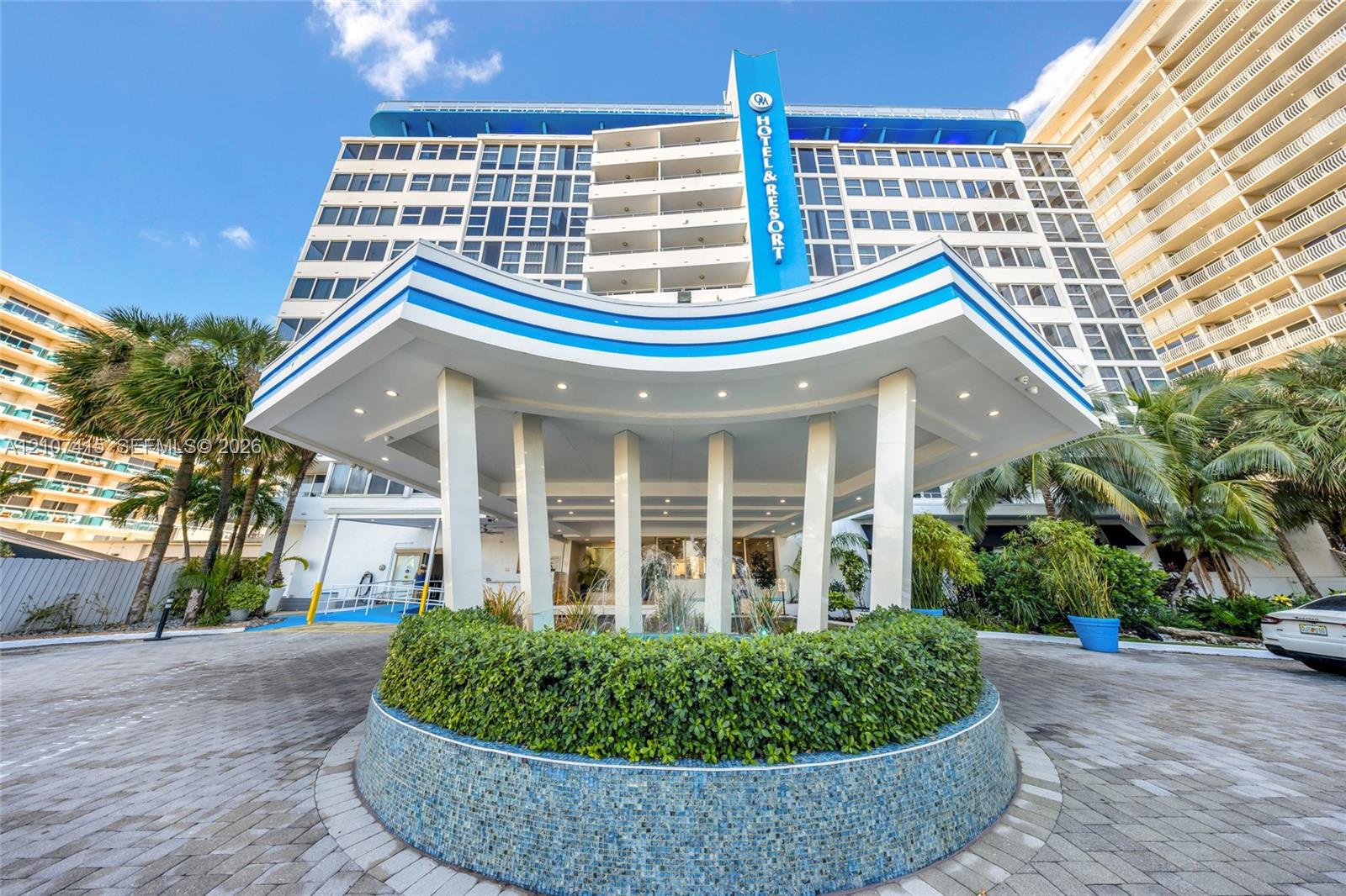 Multi-story exterior featuring a prominent porte-cochre, paved motor court, central circular landscaping, and mosaic tile exterior accents