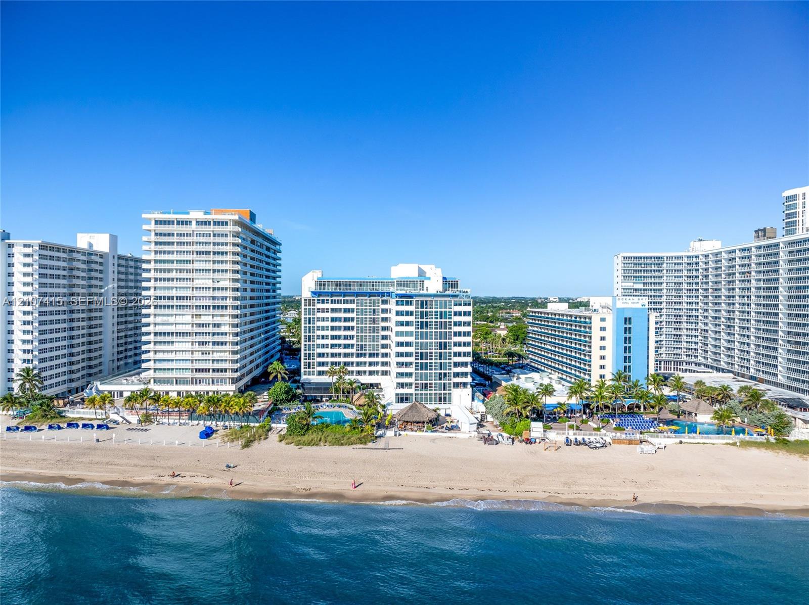 High-rise coastal architecture situated directly along a sandy shoreline with outdoor swimming pools and tropical palm tree landscaping