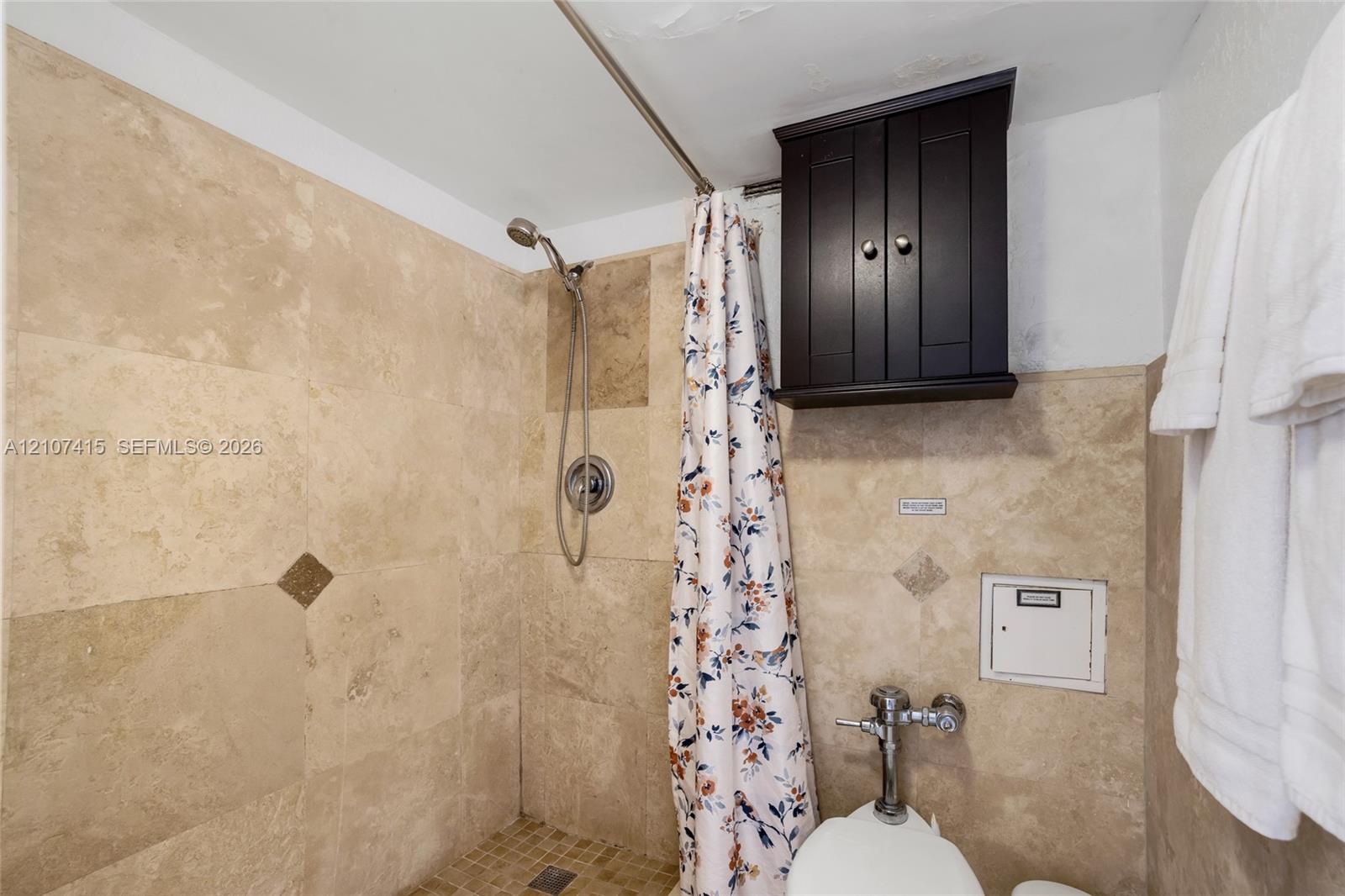 Shower enclosure featuring floor-to-ceiling stone-tile surround, mosaic tile flooring, built-in dark wood-finish cabinetry, and stainless steel hardware