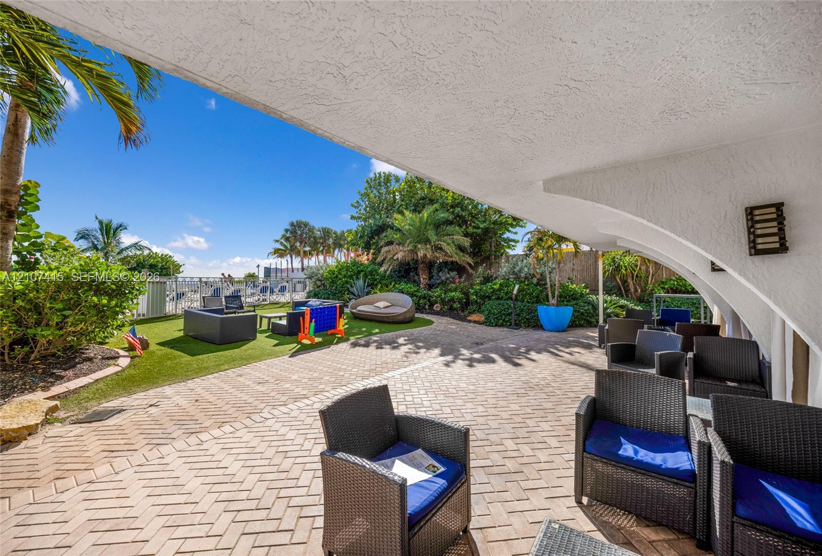 Covered concrete patio with herringbone-patterned pavers, textured stucco ceiling, and wall-mounted exterior lighting