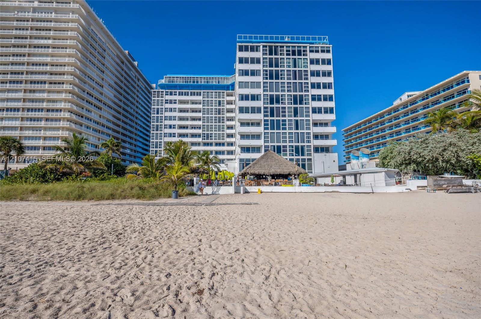 Multi-story residential high-rise complex featuring private balconies, direct beach access, and a thatched-roof cabana structure