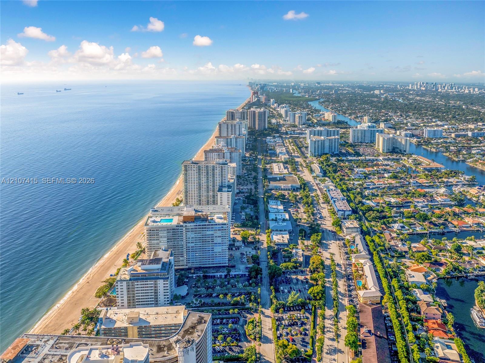 Aerial coastal perspective featuring a sandy beach, expansive ocean shoreline, high-rise residential architecture, and inland canal systems
