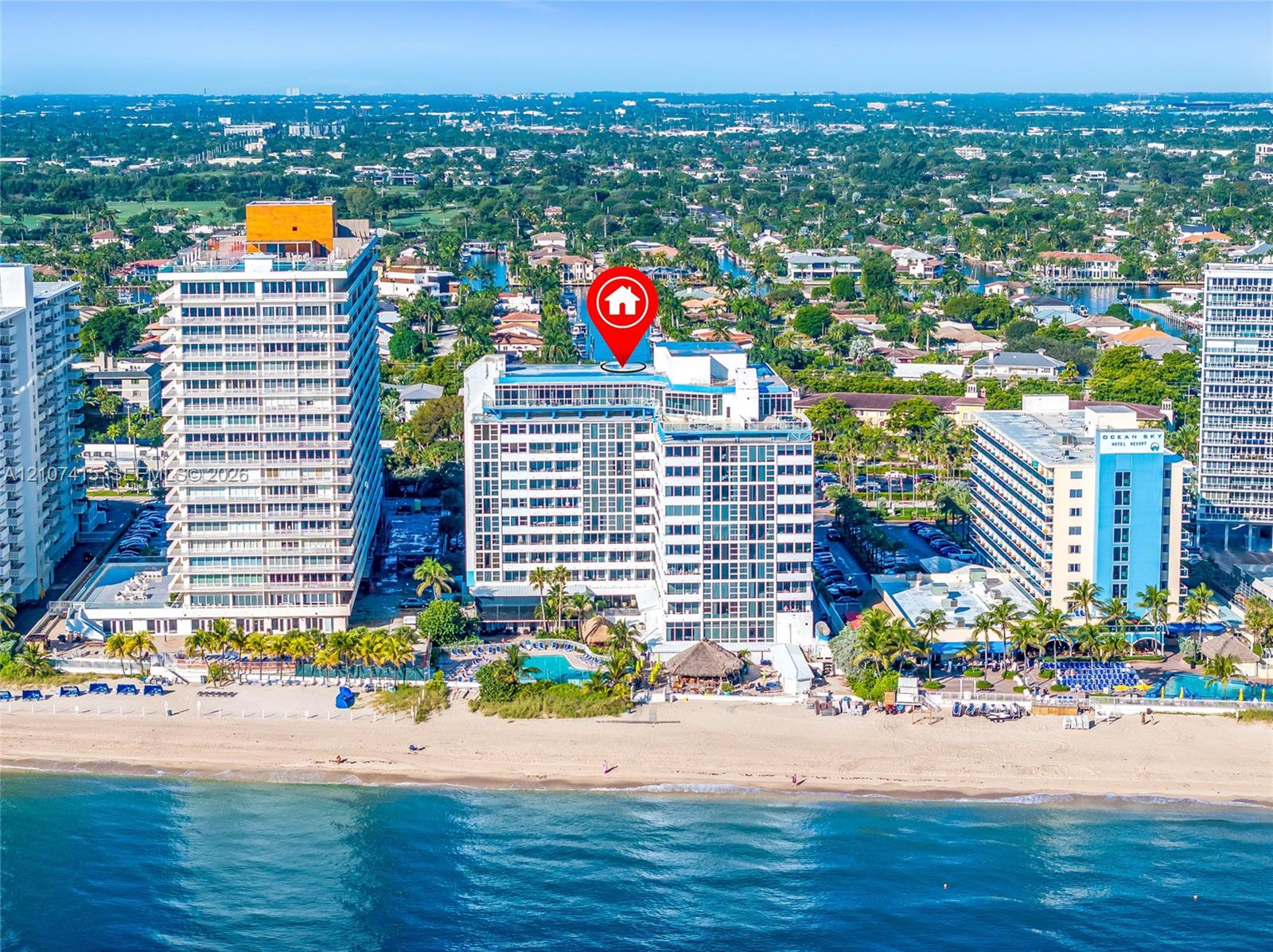 High-rise oceanfront condominium building featuring a multi-story exterior, glass balconies, ground-level swimming pool, and direct beach access