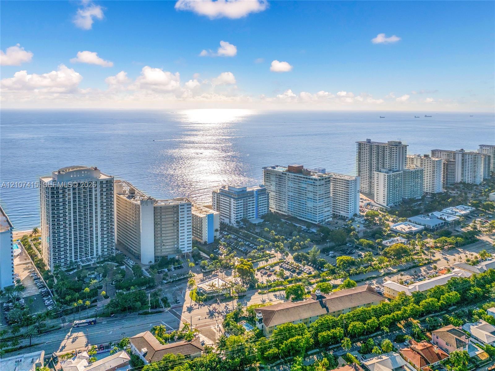 Aerial perspective of coastal landscape featuring oceanfront high-rise structures, extensive shoreline, and mature tropical vegetation