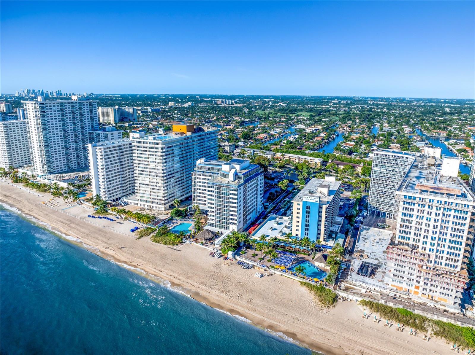 Aerial perspective of high-rise structures featuring direct beachfront positioning, shoreline access, and outdoor swimming pools