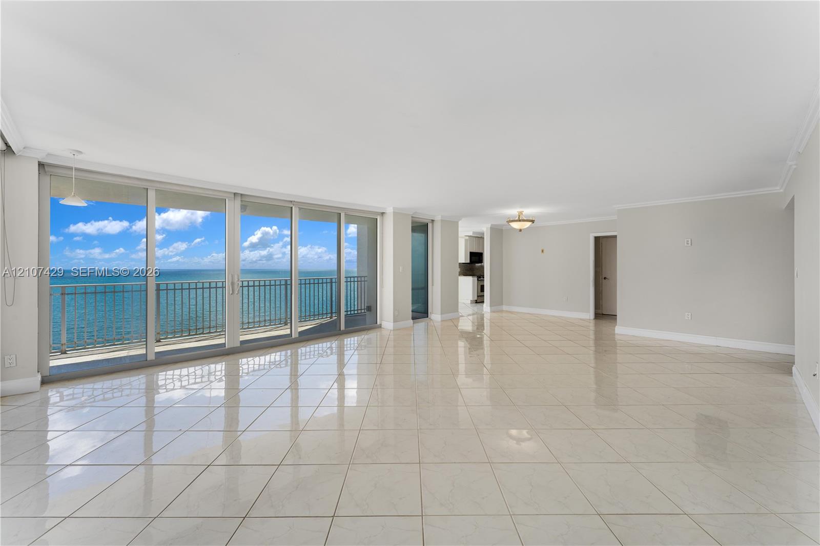 Expansive living area featuring polished tile flooring, floor-to-ceiling sliding glass doors, and a balcony with an ocean backdrop
