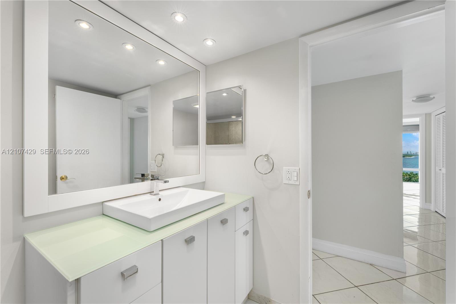 Bathroom featuring a white vanity with a glass countertop, rectangular vessel sink, wall-spanning mirror, recessed lighting, and tile flooring