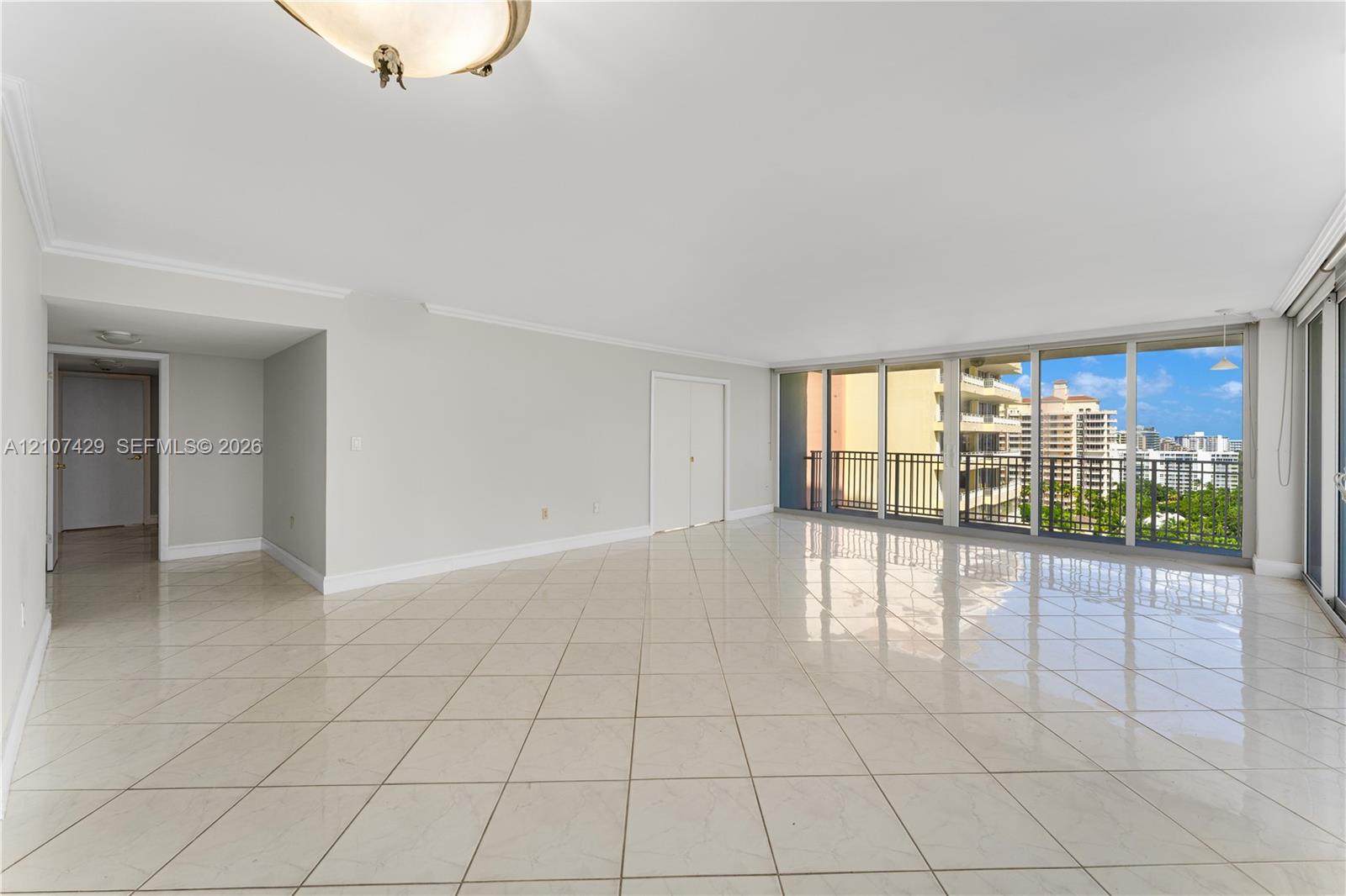 Spacious room featuring light-toned tile flooring, floor-to-ceiling glass sliding doors, and a metal balcony railing