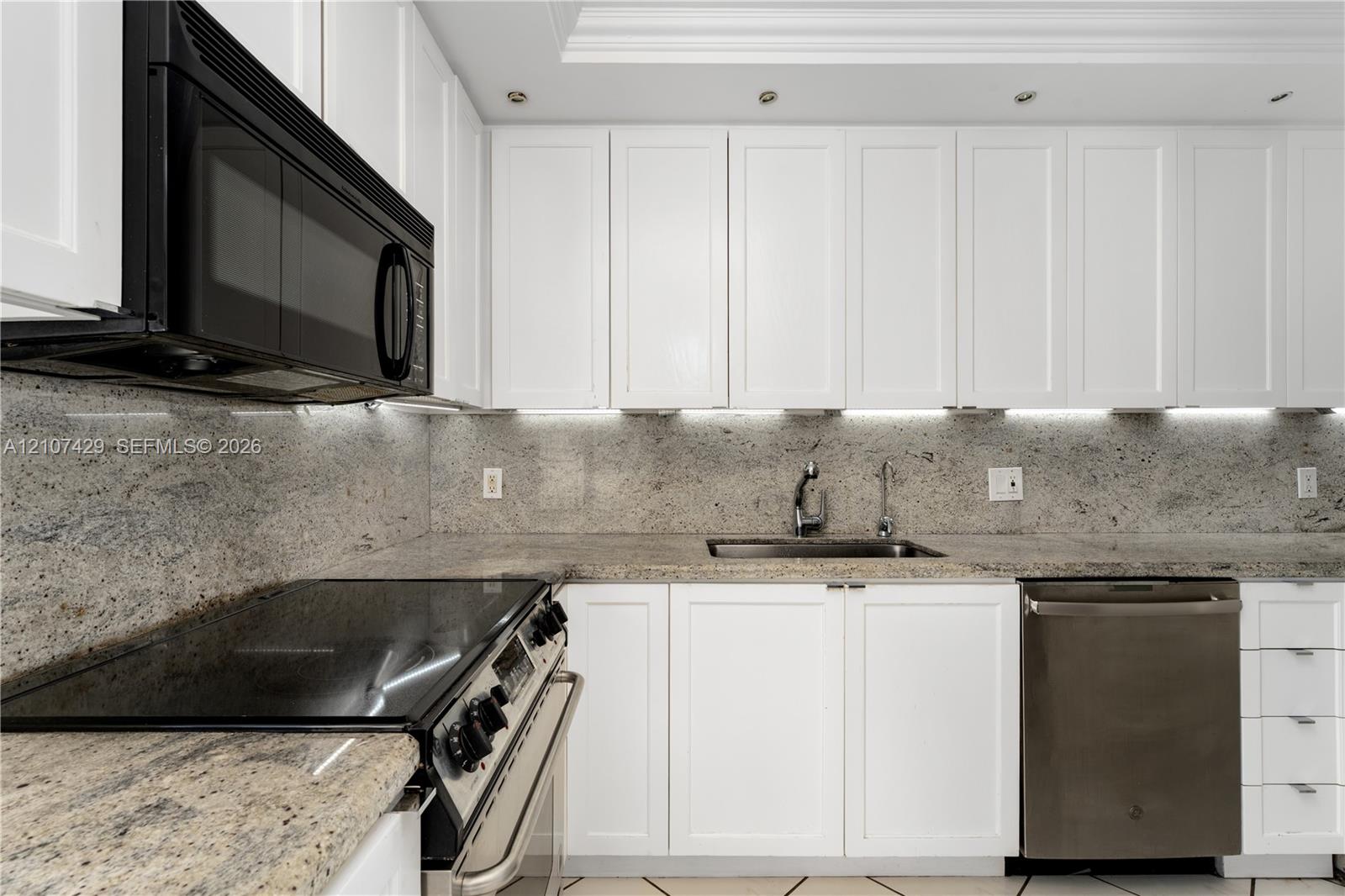 White shaker-style cabinetry, stone countertops with matching full-height backsplash, undermount sink with arched faucet, stainless steel appliances, and recessed ceiling lighting