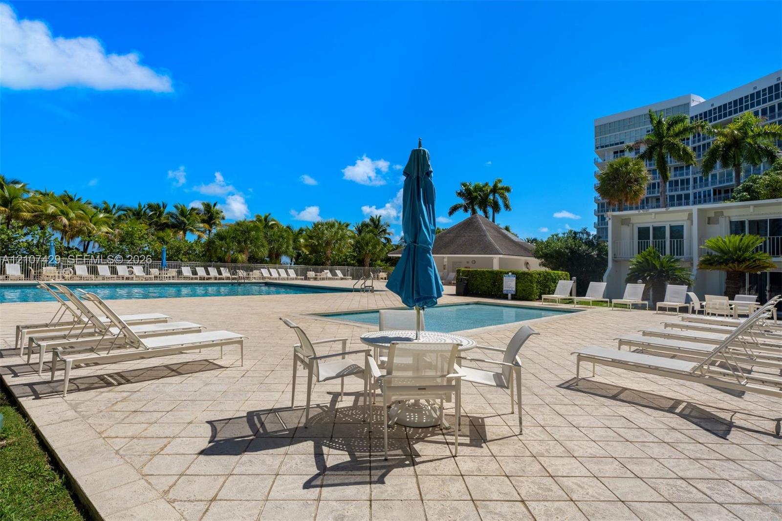 Outdoor swimming pool featuring a paved deck, surrounding palm trees, and structural shade pavilion