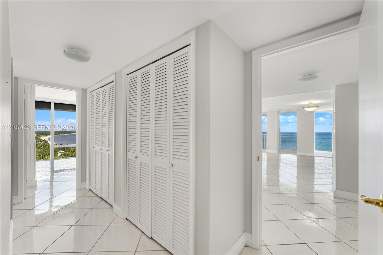 Interior hall featuring white tile flooring, floor-to-ceiling louvered closet doors, and multiple entryways showcasing direct water and shoreline scenery