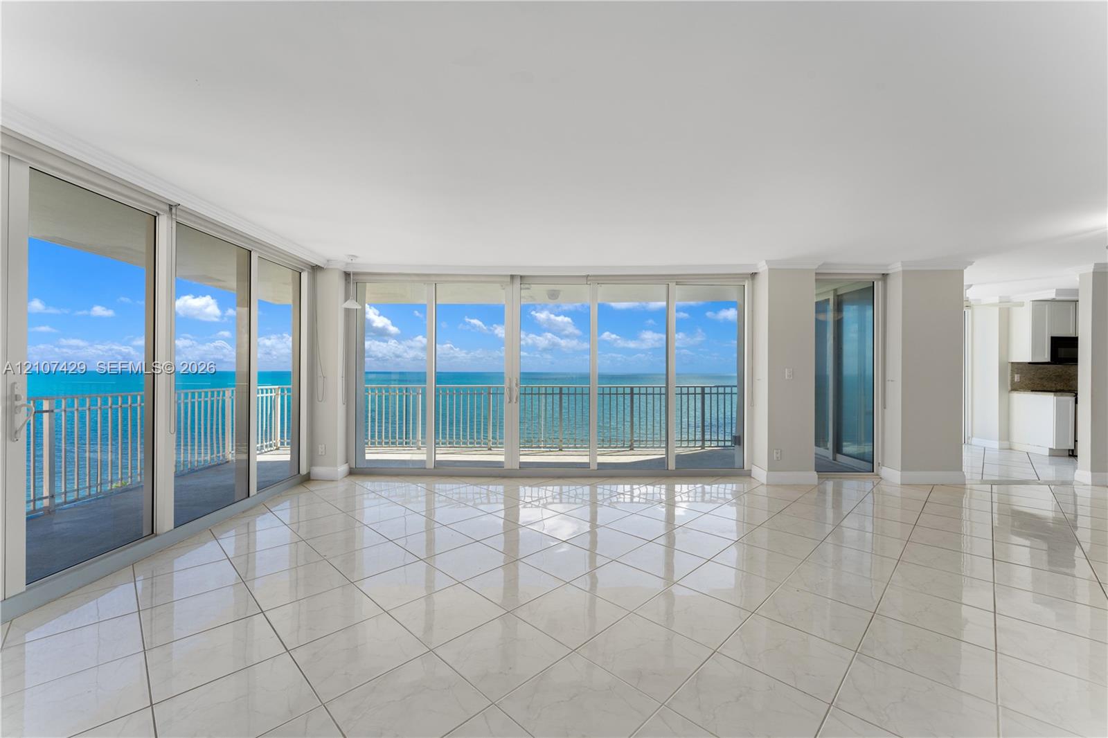 Floor-to-ceiling glass doors, expansive balcony with metal railing, polished tile flooring, and neutral wall finishes