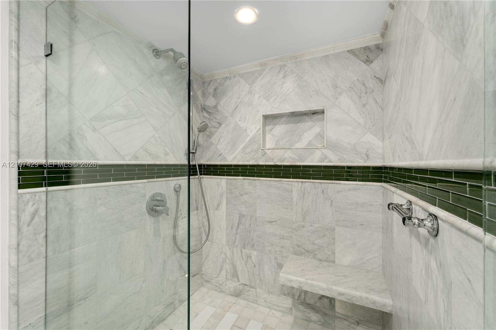 Walk-in shower featuring large-format stone tile, a built-in bench, a glass enclosure, an integrated wall niche, and a contrasting green glass tile accent border