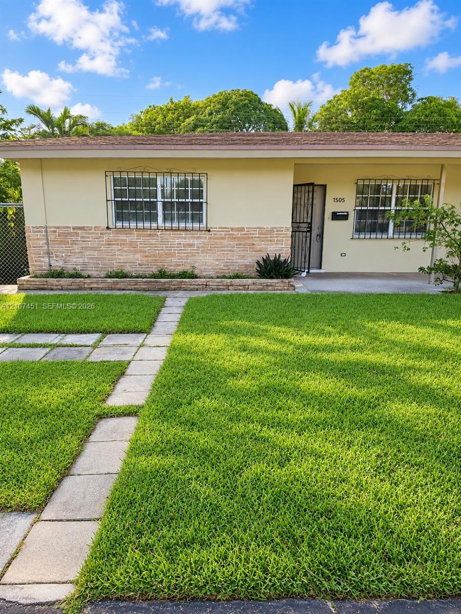 Single-story exterior featuring light-toned stucco and natural stone facade, stone-edged planter beds, concrete paver walkway, and metal window security bars