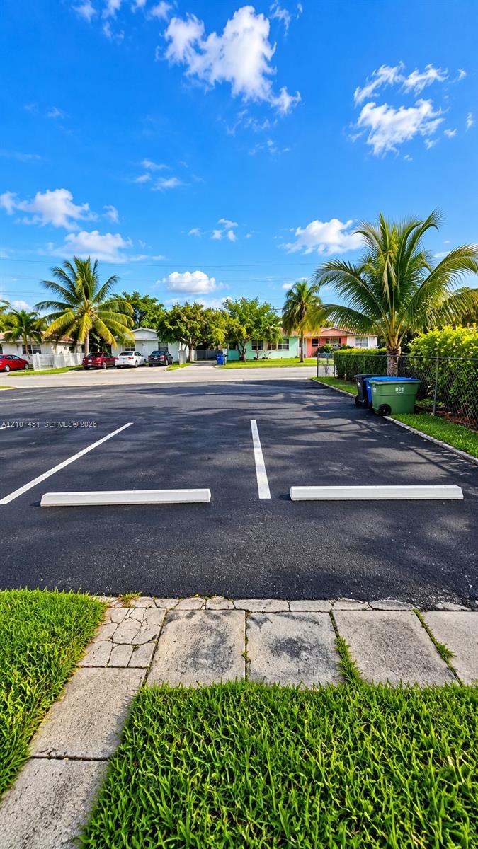 Asphalt parking area featuring marked spaces, concrete wheel stops, stone paver edging, and mature palm trees Asphalt parking area featuring marked spaces, concrete wheel stops, stone paver edging, and mature palm trees