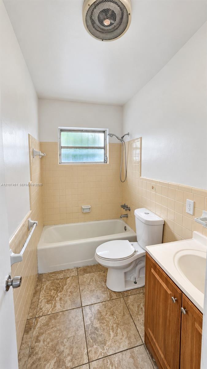 Bathroom featuring tile flooring, a porcelain bathtub with wall-mounted shower fixture, ceramic tile surround, and wood-finish vanity with an integrated sink