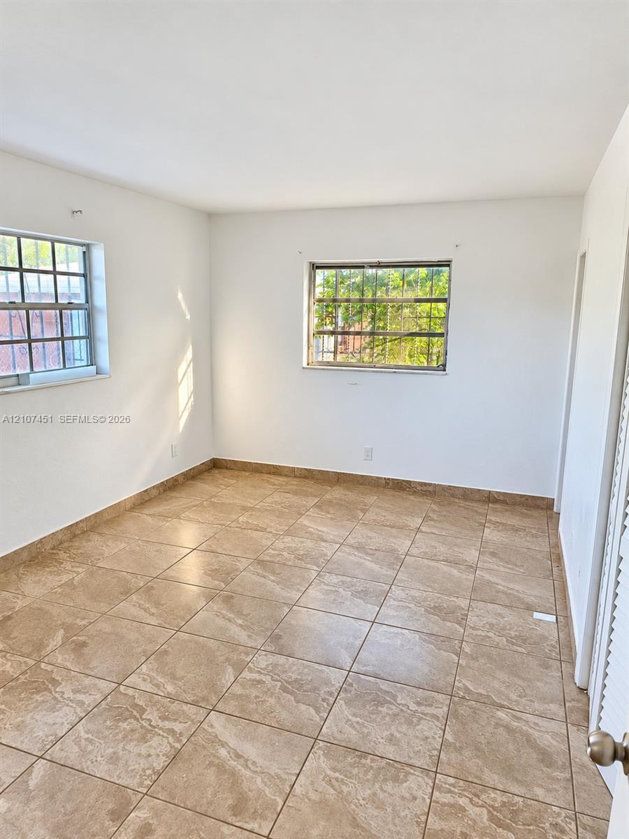 Interior space featuring neutral wall tones, large-format ceramic tile flooring, and dual windows with security bars Interior space featuring neutral wall tones, large-format ceramic tile flooring, and dual windows with security bars