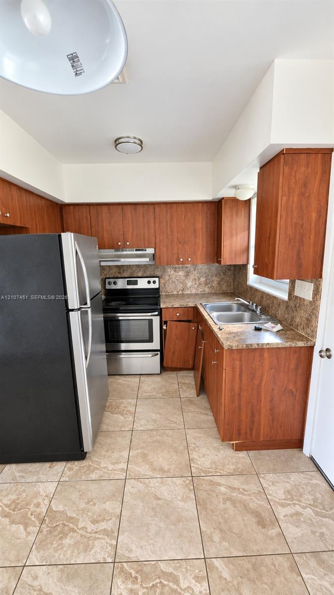 Kitchen featuring wood-finish cabinetry, stone-pattern laminate countertops, stainless steel range and refrigerator, dual-basin stainless steel sink, and ceramic tile flooring Kitchen featuring wood-finish cabinetry, stone-pattern laminate countertops, stainless steel range and refrigerator, dual-basin stainless steel sink, and ceramic tile flooring