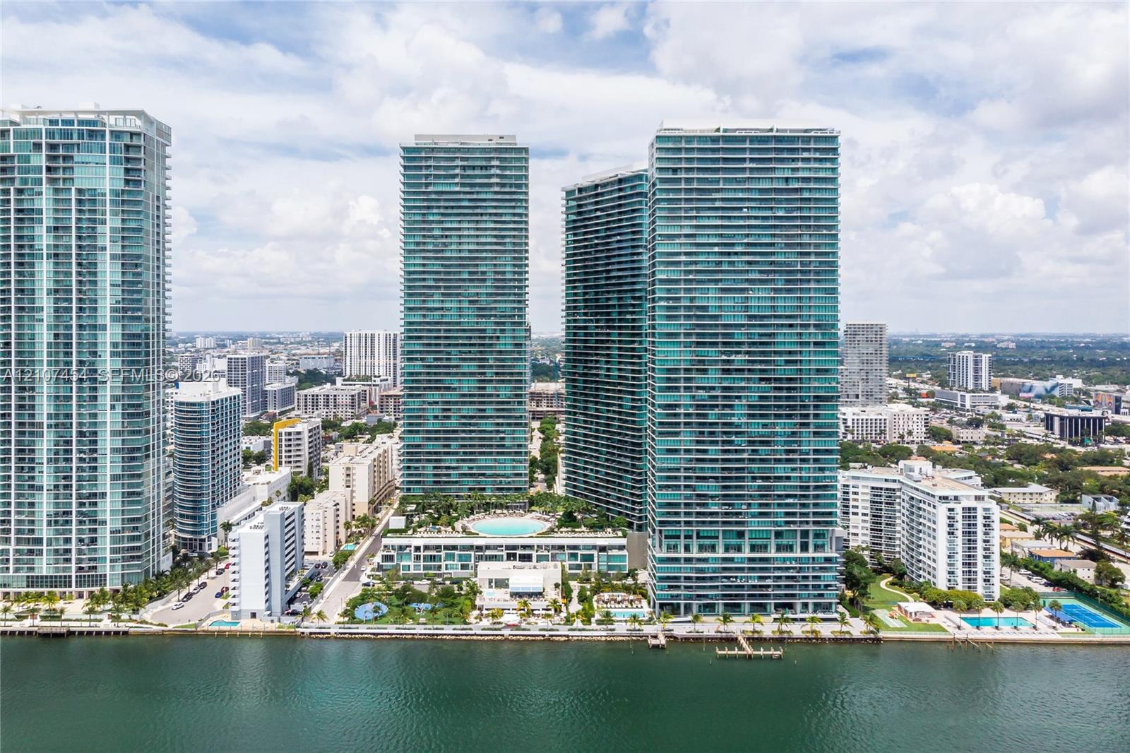 High-rise complex featuring glass-facade towers, an elevated outdoor pool, landscaped podium deck, and direct waterfront placement