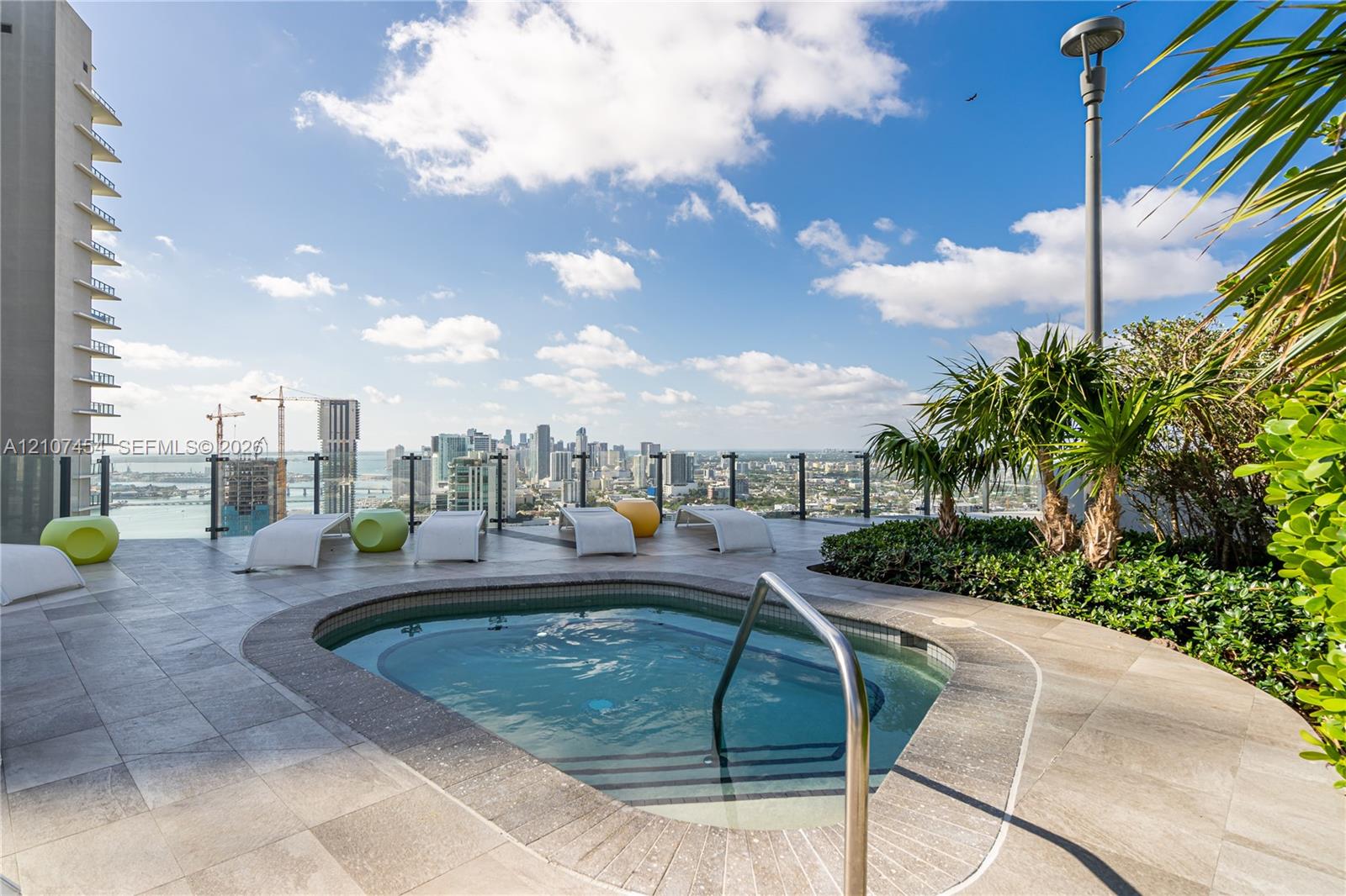 Rooftop terrace featuring a built-in spa, stone-tile decking, glass panel railing, and integrated landscaping