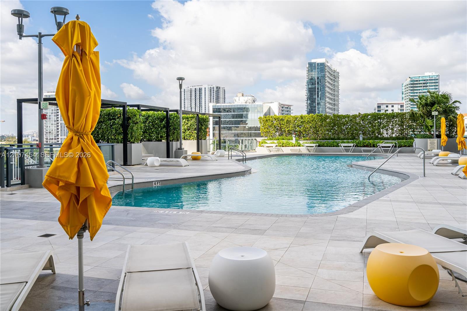 Rooftop pool featuring light-toned tile decking, integrated metal pergolas, manicured hedge privacy screening, and stainless steel pool railings